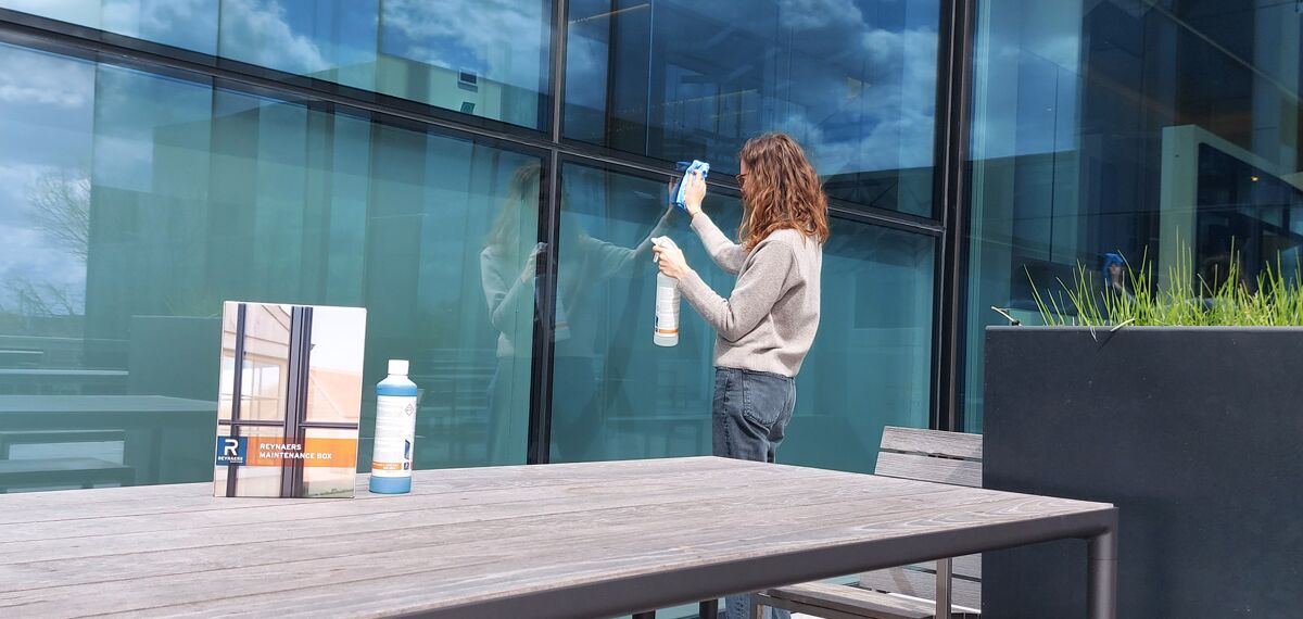 Woman cleaning aluminium window wall with specialised care products.